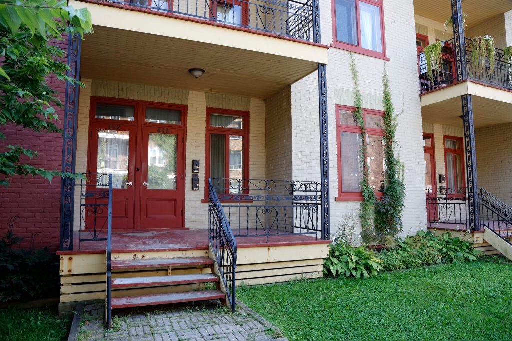 Charming ground floor apartment entrance with red doors, a small porch, and green lawn — ideal for those considering the benefits of ground floor living.