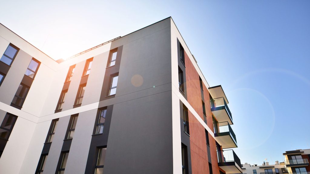 Modern mid-rise apartment building under clear blue sky, illustrating the appeal of top floor apartments with private balconies and sunlit views.