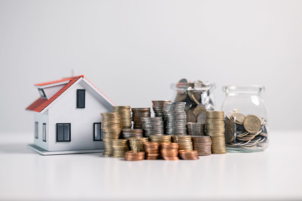 House model with stacked coins and jars representing real estate investing and financial growth.